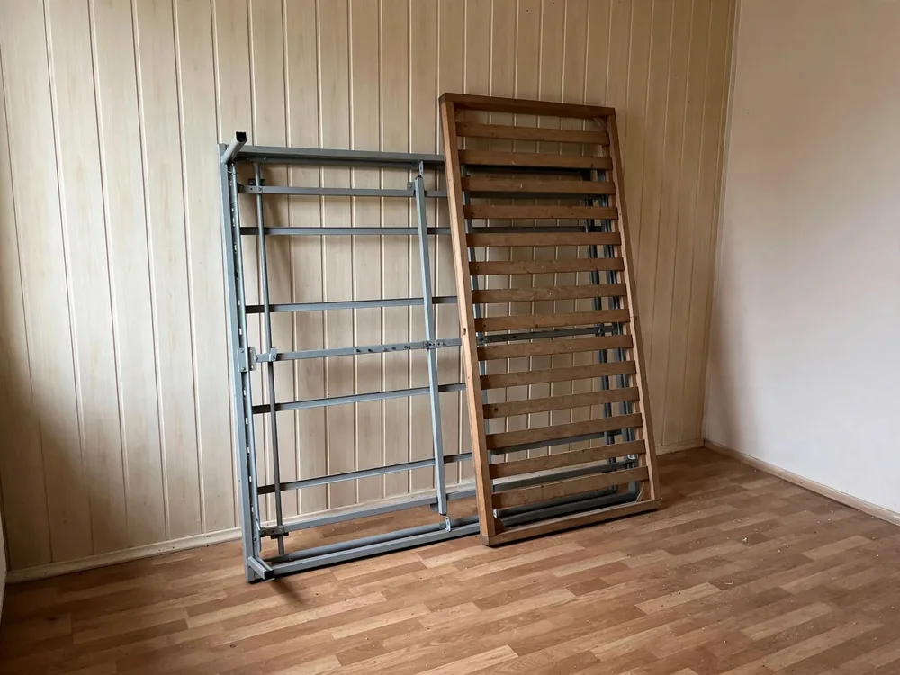 Metalowy i drewniany stelaż łóżka oparte o ścianę w pustym pokoju