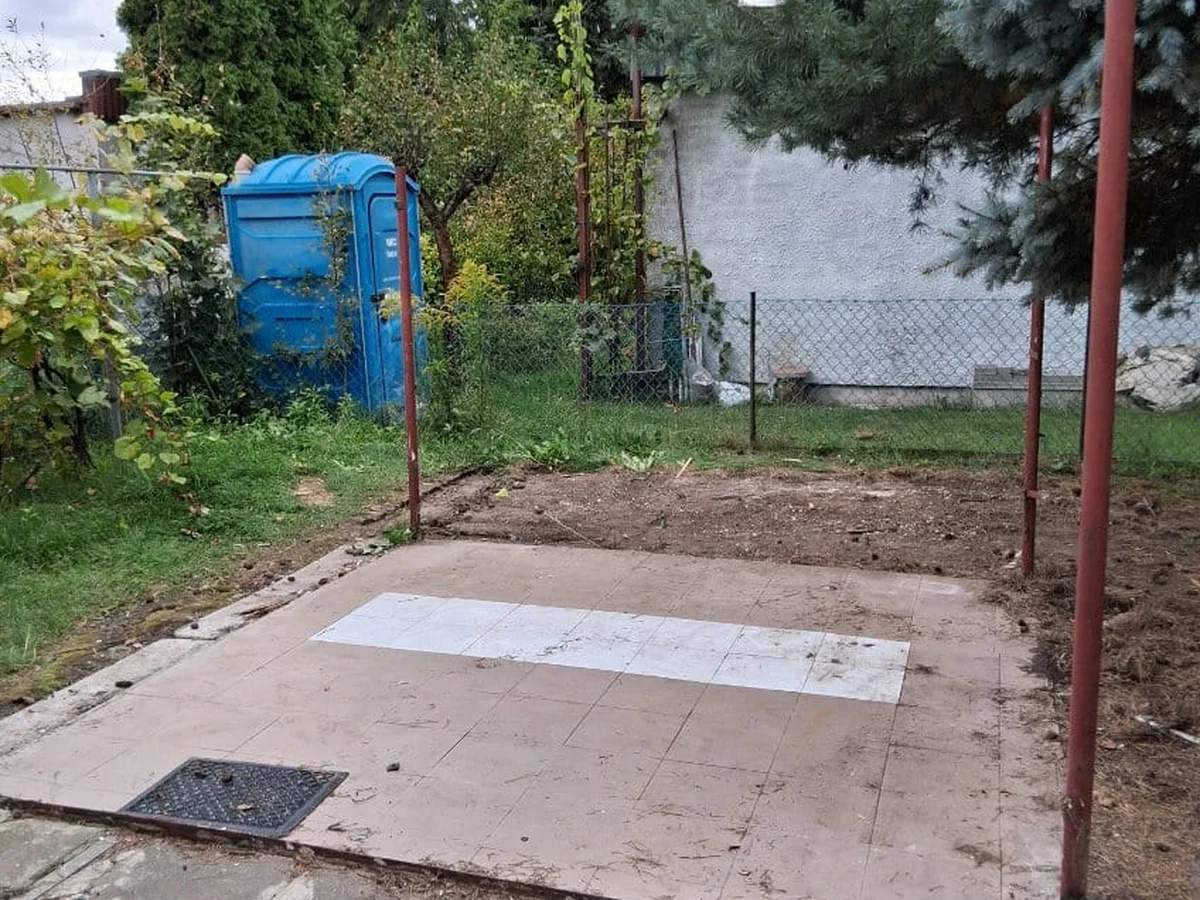 Pusta, zamieciona posadzka z płytek na działce po wywiezieniu rzeczy, w tle przenośna toaleta