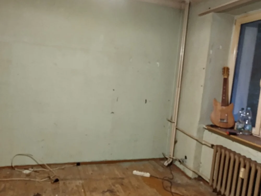 Opróżniony pokój z grzejnikiem pod oknem i gitarą na parapecie